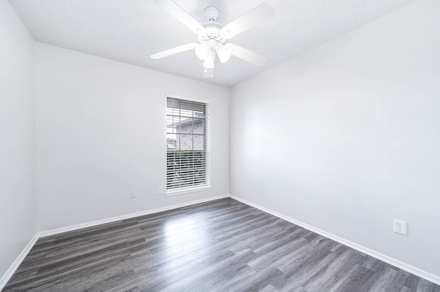 empty room with dark wood finished floors, a ceiling fan, and baseboards