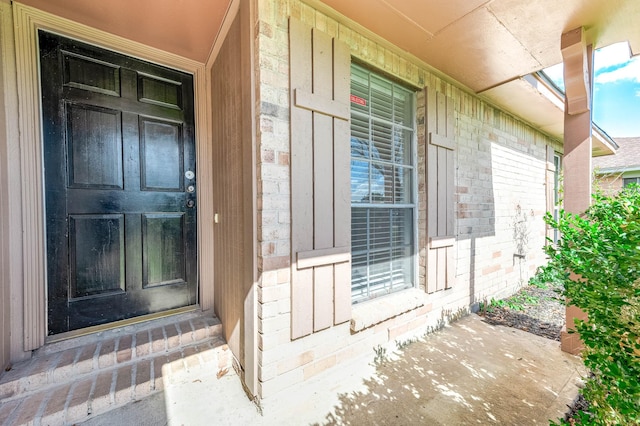 entrance to property featuring a porch and brick siding