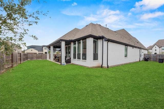 rear view of property with a fenced backyard, a shingled roof, a lawn, and brick siding