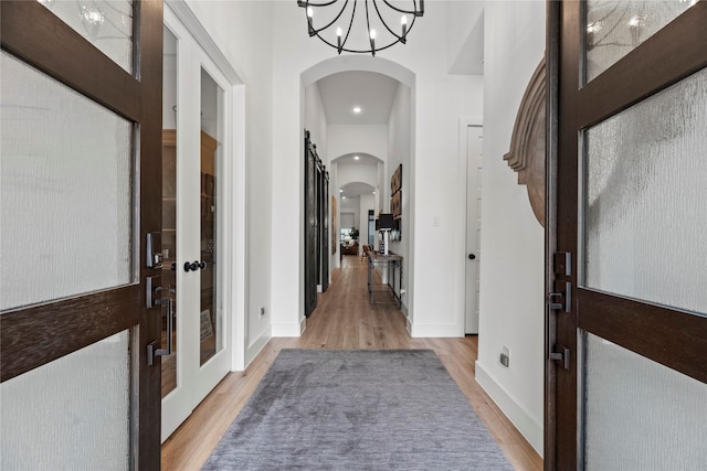 entrance foyer featuring light wood finished floors, baseboards, arched walkways, and an inviting chandelier