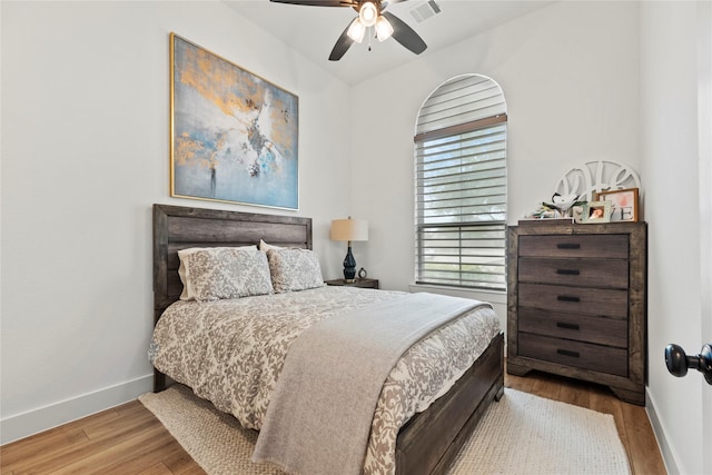 bedroom with a ceiling fan, visible vents, baseboards, and wood finished floors