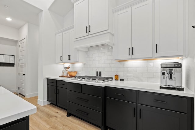 kitchen featuring decorative backsplash, light countertops, light wood-style floors, white cabinetry, and stainless steel gas cooktop