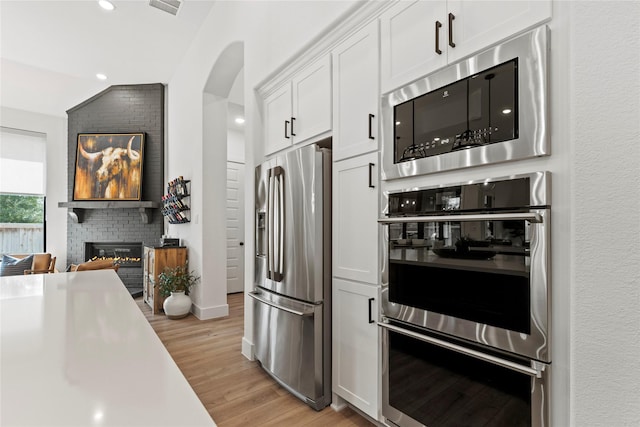 kitchen featuring stainless steel appliances, light wood-style floors, a fireplace, white cabinetry, and recessed lighting