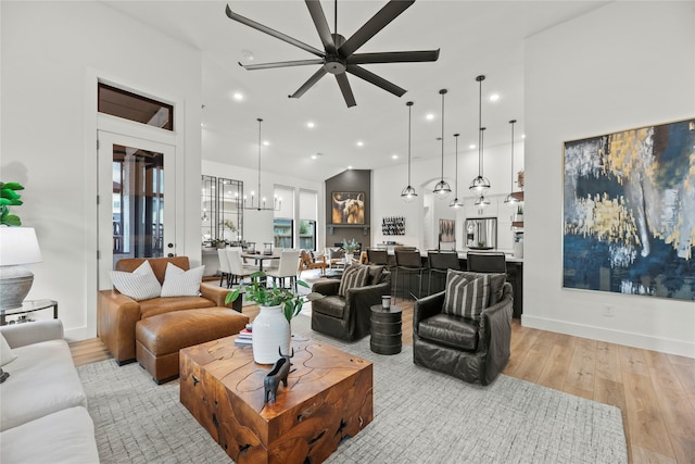 living room featuring baseboards, light wood-type flooring, a towering ceiling, and recessed lighting