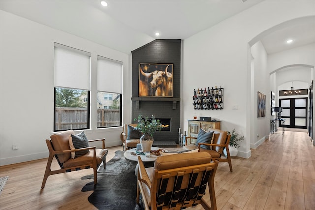 living area with arched walkways, vaulted ceiling, a fireplace, and light wood-style floors