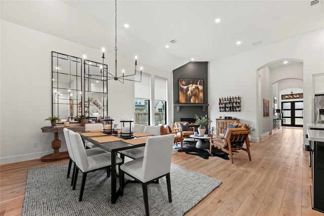 dining area featuring light wood finished floors, baseboards, arched walkways, lofted ceiling, and a fireplace