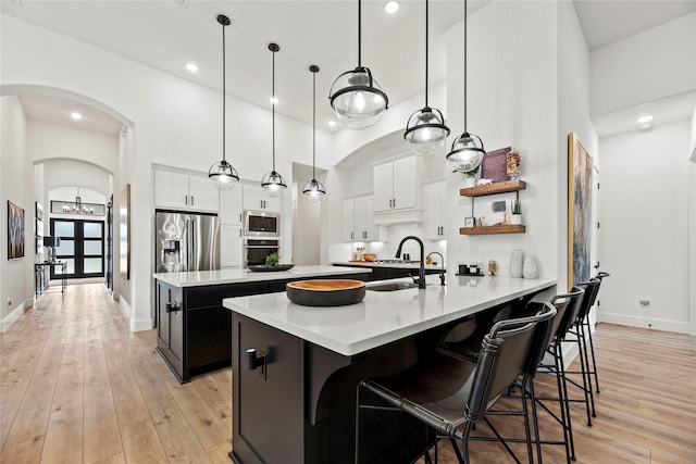 kitchen with arched walkways, light wood-style flooring, a towering ceiling, light countertops, and appliances with stainless steel finishes