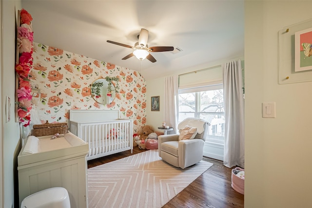 bedroom with visible vents, wallpapered walls, a nursery area, and wood finished floors