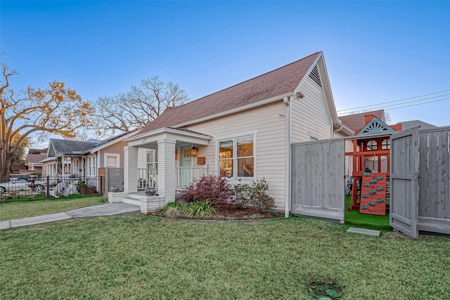 view of front of home with a playground, a front yard, and fence