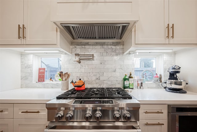 kitchen featuring stainless steel gas range oven, tasteful backsplash, light countertops, exhaust hood, and white cabinetry