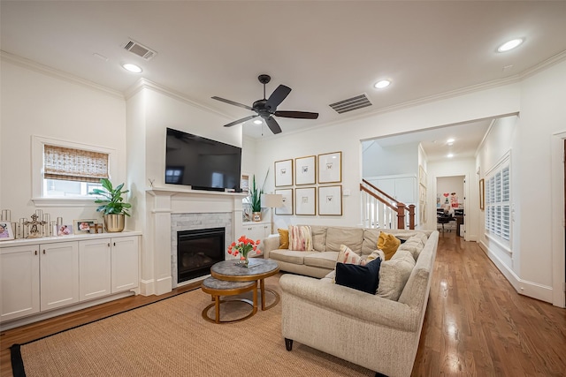 living area featuring visible vents, light wood-style flooring, a ceiling fan, and a glass covered fireplace