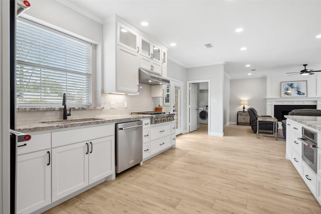 kitchen featuring stainless steel appliances, washer / clothes dryer, white cabinets, a sink, and under cabinet range hood