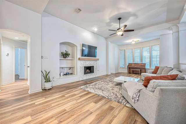 living area with light wood-style flooring, visible vents, baseboards, built in features, and a tiled fireplace