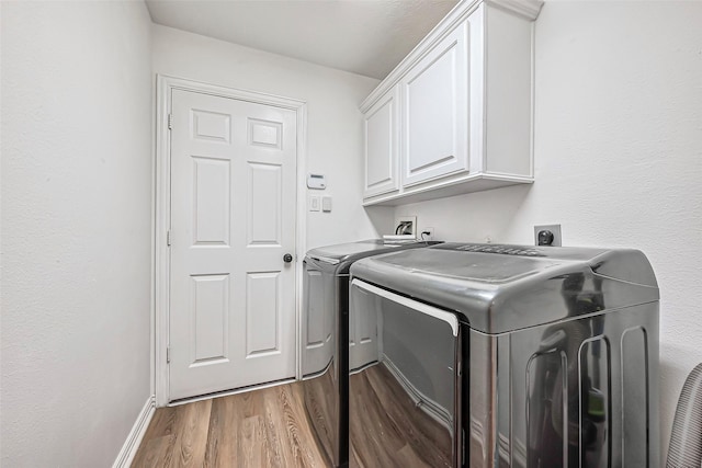 clothes washing area featuring light wood-style floors, cabinet space, washer and clothes dryer, and baseboards