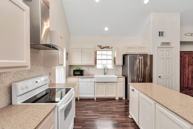 kitchen with white appliances, visible vents, lofted ceiling, wall chimney range hood, and a sink