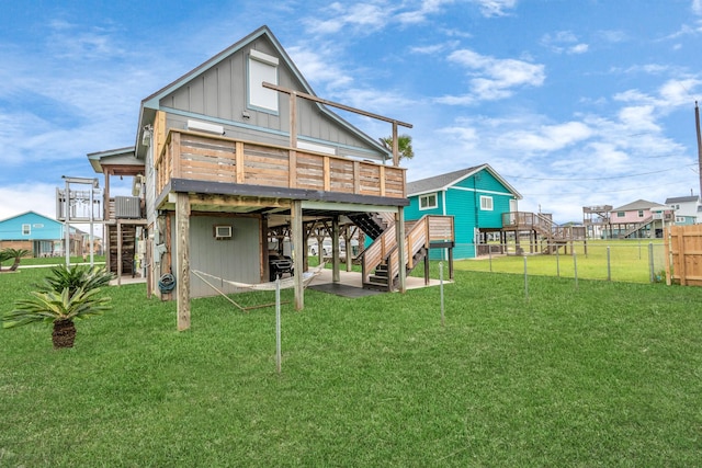 back of house featuring a lawn, board and batten siding, fence, a deck, and stairs