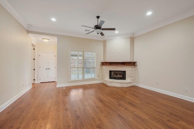 unfurnished living room featuring baseboards, ornamental molding, wood finished floors, and a stone fireplace