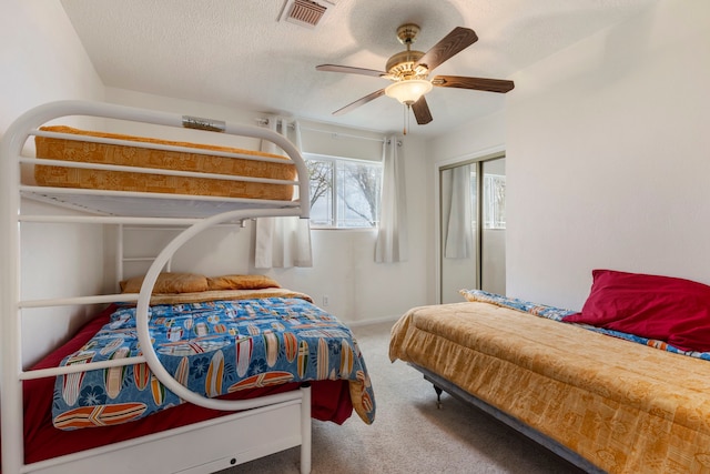 carpeted bedroom with a textured ceiling, visible vents, baseboards, a ceiling fan, and a closet