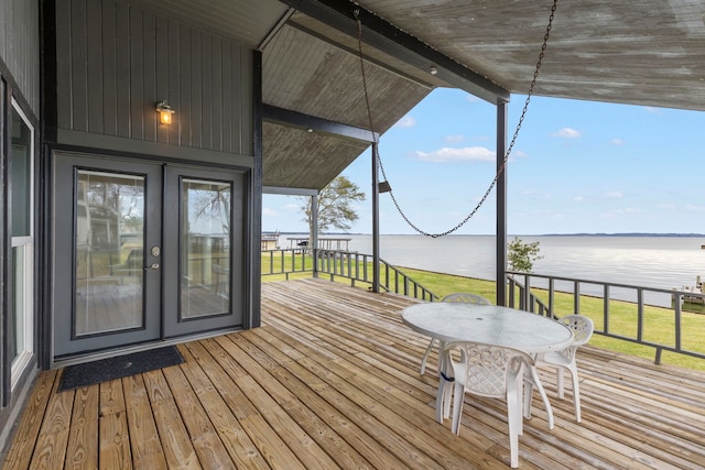 wooden terrace with outdoor dining space, a lawn, and a water view