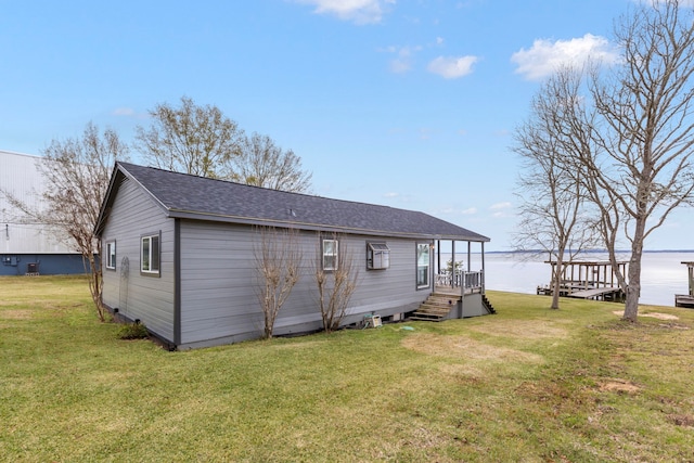 back of property featuring a water view, a lawn, and roof with shingles