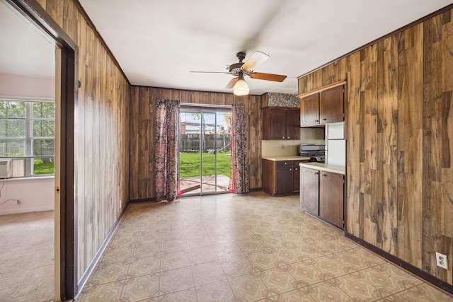 kitchen featuring stainless steel stove, wooden walls, a ceiling fan, baseboards, and light countertops