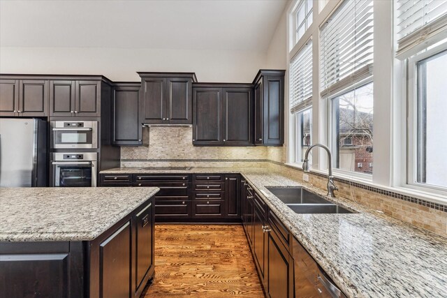 kitchen featuring stainless steel appliances, decorative backsplash, light wood-style floors, a sink, and light stone countertops