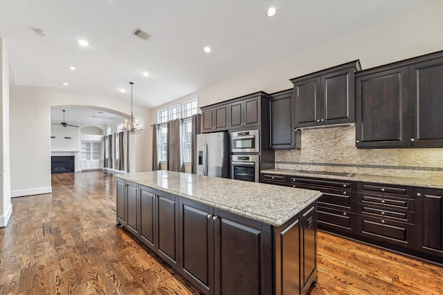 kitchen featuring visible vents, backsplash, a kitchen island, arched walkways, and stainless steel appliances