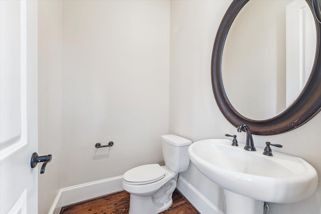 half bath with a sink, toilet, baseboards, and wood finished floors