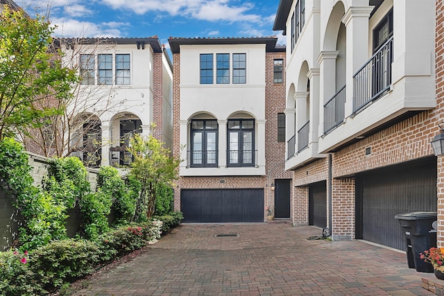 view of front of property with decorative driveway, brick siding, a garage, and stucco siding