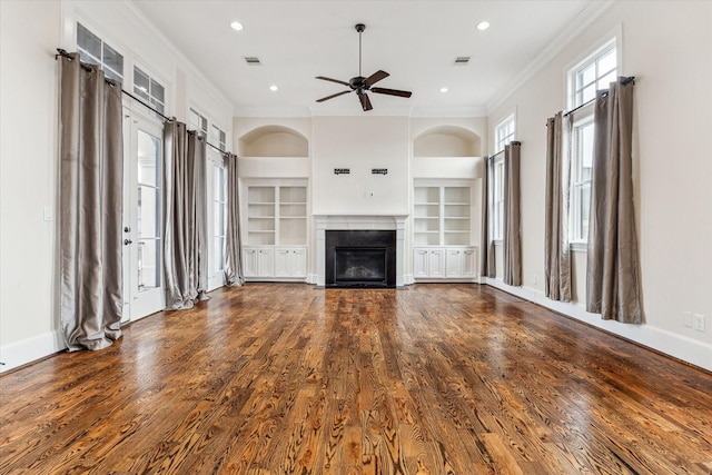 unfurnished living room with built in features, ornamental molding, wood finished floors, and a glass covered fireplace