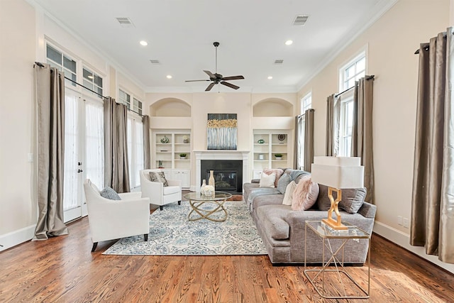 living room featuring visible vents, built in features, crown molding, and wood finished floors