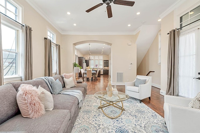 living area with visible vents, arched walkways, wood finished floors, and crown molding