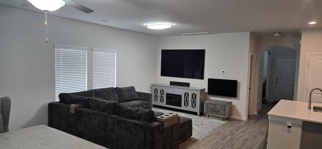 living area with arched walkways, light wood finished floors, baseboards, and a ceiling fan