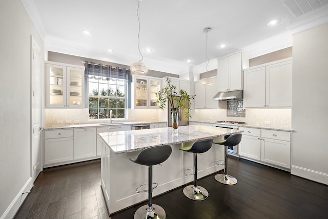 kitchen featuring under cabinet range hood, a kitchen island, white cabinetry, and crown molding