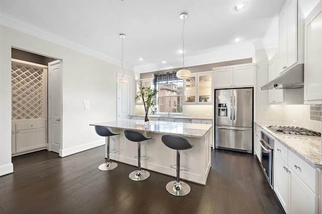 kitchen with dark wood finished floors, stainless steel appliances, backsplash, white cabinetry, and under cabinet range hood