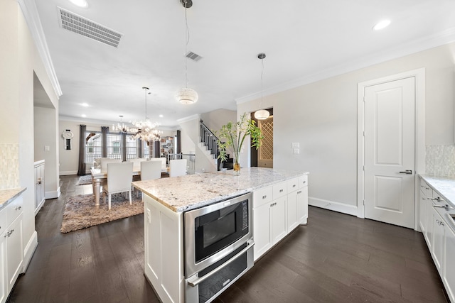 kitchen featuring visible vents, dark wood finished floors, stainless steel microwave, crown molding, and white cabinetry