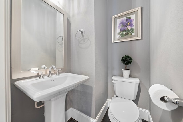 bathroom with a textured wall, a sink, and toilet