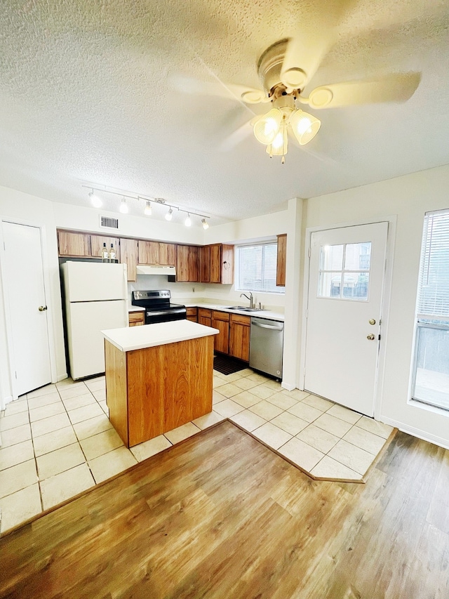 kitchen with brown cabinetry, appliances with stainless steel finishes, light countertops, under cabinet range hood, and a sink