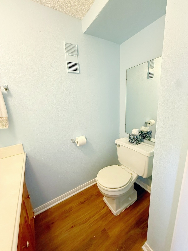 half bath with toilet, wood finished floors, vanity, visible vents, and baseboards