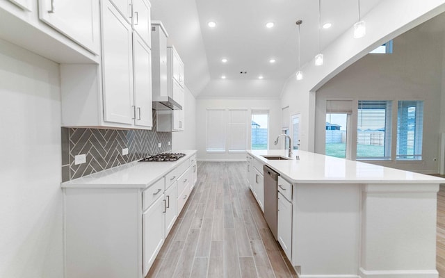 kitchen featuring light wood finished floors, decorative backsplash, stainless steel appliances, wall chimney range hood, and a sink