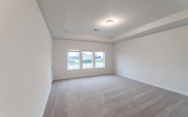 carpeted spare room with a raised ceiling, visible vents, and baseboards