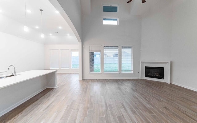 unfurnished living room featuring a fireplace, visible vents, a high ceiling, a ceiling fan, and light wood-type flooring