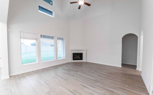 unfurnished living room with ceiling fan, arched walkways, light wood-style flooring, a fireplace, and baseboards