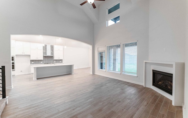 unfurnished living room with ceiling fan, light wood-type flooring, a glass covered fireplace, and baseboards