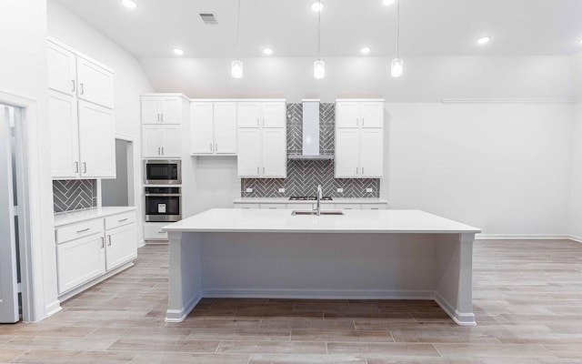 kitchen featuring a kitchen island with sink, stainless steel appliances, white cabinets, light countertops, and light wood finished floors