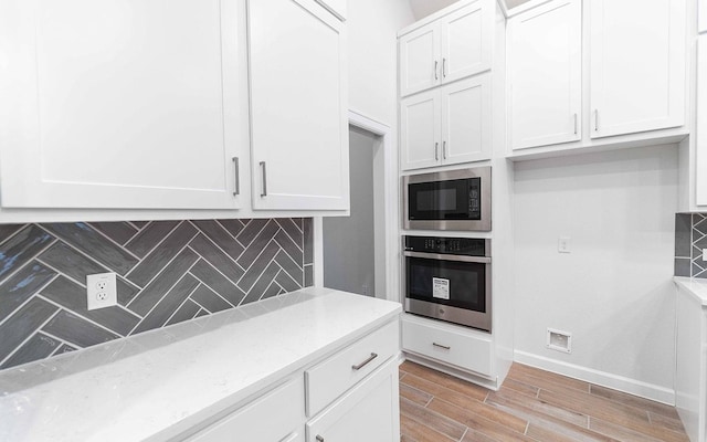 kitchen with light wood finished floors, decorative backsplash, white cabinetry, stainless steel oven, and built in microwave