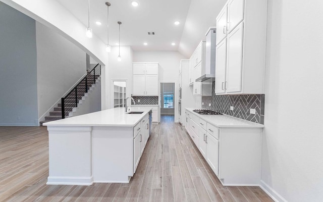 kitchen with stainless steel gas stovetop, light wood-style floors, white cabinets, a sink, and wall chimney exhaust hood