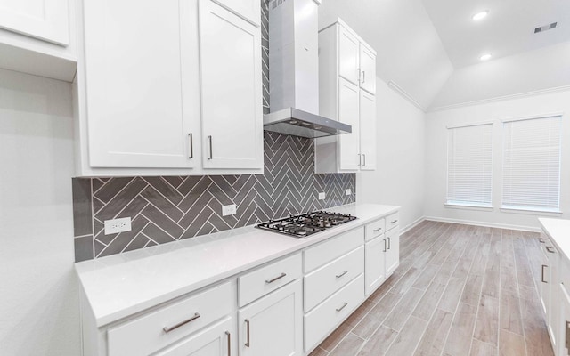 kitchen featuring stainless steel gas cooktop, light wood-style flooring, decorative backsplash, white cabinetry, and wall chimney range hood