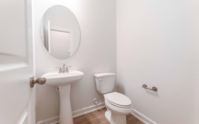 half bath with toilet, wood tiled floor, and baseboards