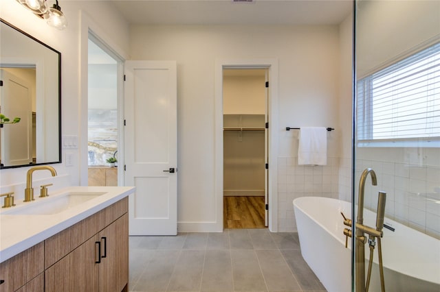 full bathroom with tile patterned flooring, a spacious closet, a freestanding bath, vanity, and tile walls